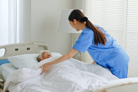 hospice care worker tucks a female patient into bed