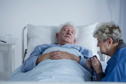 woman praying at the bedside of a hospice patient