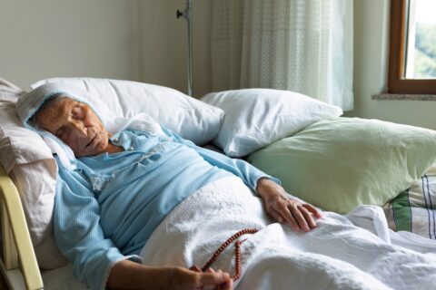 A woman in hospice care at home holds prayer beads near the end of her life in Portland