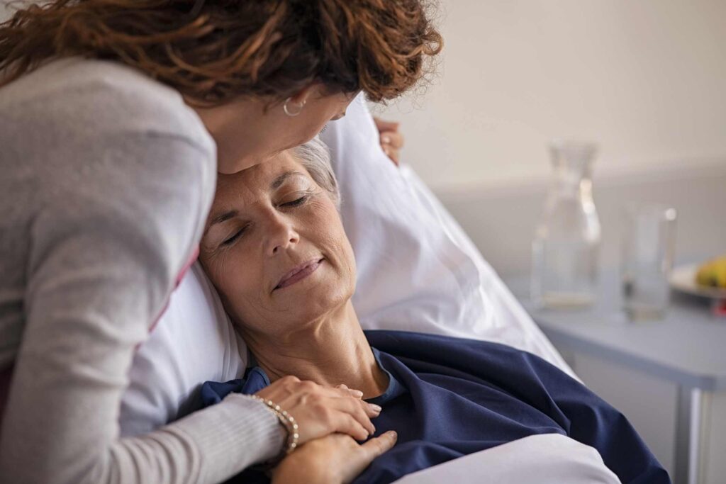 Older adult resting in a hospice bed with a caregiver offering comfort in Portland, OR